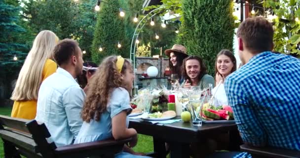 Many mixed race young people sitting at table and talking in garden. African American and Caucasian beautiful girls smiling outdoor. Joyful Asian girl and handsome males chatting. Celebration concept — Stock Video