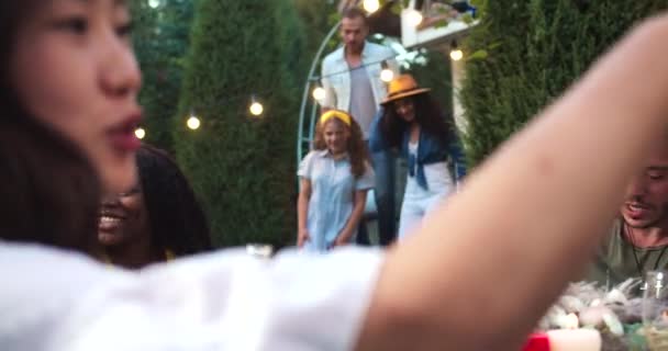 在花园派对上，许多年轻快乐的男女混血朋友在一起玩得很开心。非洲裔美国女孩抱着白种人快乐美丽的女人戴帽子。庆祝概念 — 图库视频影像