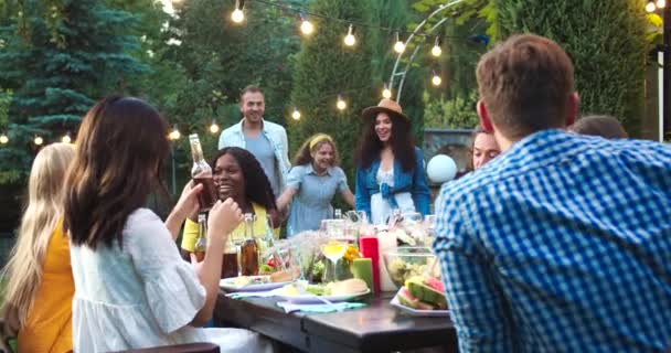 Mladí míšenci se scházejí a baví se na zahradním večírku. Afroameričanky a kavkazské krásné dívky objímají. Radostná asijská dívka s pitím. Volný čas. Koncept Summertime Friendship — Stock video
