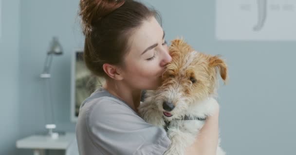 关闭女兽医抱着狗的肖像，在诊所检查后等待主人时亲吻它。身着西服的兽医。宠物护理、兽医、健康动物概念. — 图库视频影像