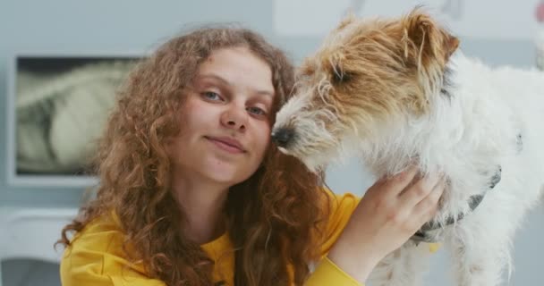 Primer plano sonriente dueño del perro, hermosa chica rizada en suéter amarillo, la celebración de mascotas en la cita con los médicos en la clínica veterinaria y mirando a la cámara. Concepto de cuidado de mascotas, veterinario. — Vídeo de stock