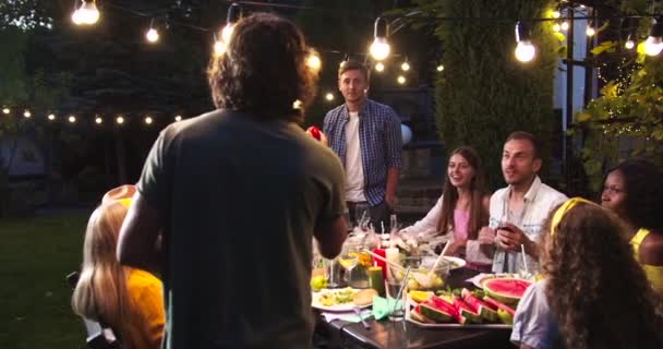 Gente alegre de raza mixta divirtiéndose y jugando en la fiesta del jardín por la noche. Niños y niñas caucásicos bebiendo y hablando. Chica afroamericana sonriendo. Asiática mujer riendo Summertime divertido concepto — Vídeos de Stock