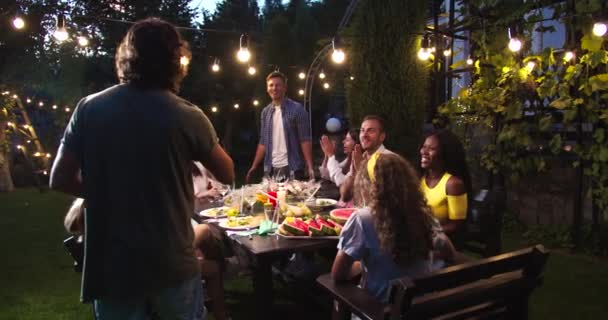 多民族快乐的人们在晚上的花园派对上玩得很开心。白人男孩和女孩喝酒和说话。非裔美国人和亚裔女性大笑。派对游戏。有趣的概念 — 图库视频影像