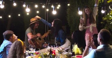 Neşeli çoklu etnik kökenli genç arkadaşlar yaz akşamları bahçede eğleniyor ve alkışlıyorlar. Beyaz bir adam gitar çalıyor ve dışarıda şarkı söylüyor. Afro-Amerikalı ve Asyalı kızlar gülümsüyor.