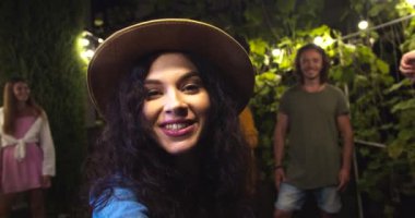 Kameraya konuşan şapkalı mutlu beyaz bir kız. Güzel Afrikalı Amerikalı ve Asyalı kızlar el sallıyor. Yakışıklı, neşeli adamlar gülümsüyor. Akşamki bahçe partisinde melez arkadaşlar. Eğlenceli konsept