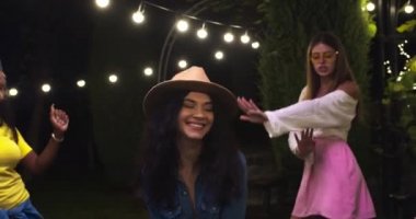 Partide bahçede dans eden beyaz şapkalı güzel bir kızı yakından çek. Afro-Amerikalı neşeli kadın eğleniyor. Neşeli melez kızlar müzik dinliyorlar. Yaz akşamı. Eğlenceli konsept