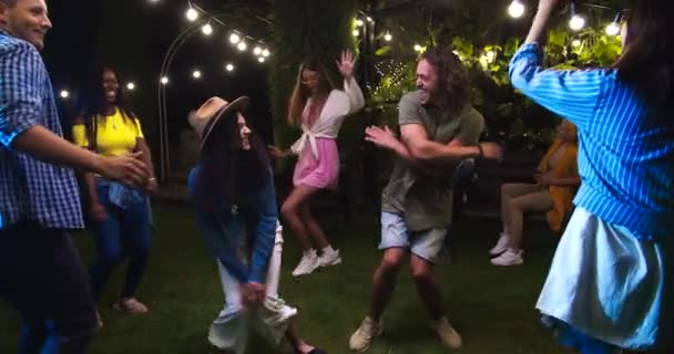 Feliz hermosa mezcla de razas chicas bailando en el jardín en la fiesta. Chica caucásica en sombrero y chico haciendo movimientos divertidos. Danza femenina afroamericana. Un tipo feliz moviéndose a la música. Concepto de celebración — Vídeos de Stock