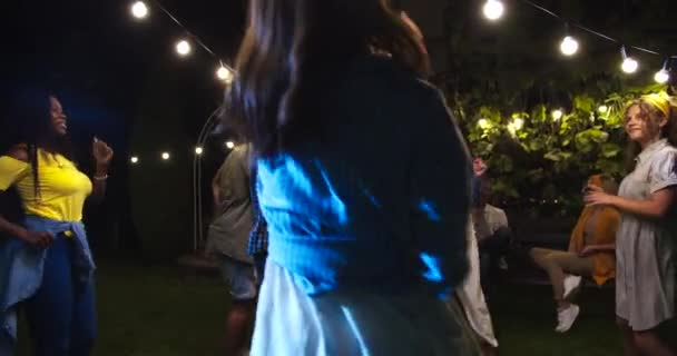 Szczęśliwe mieszane dziewczyny tańczące w nocy na podwórku. Biała dziewczyna i chłopak robiący zabawne ruchy. Afroamerykanki tańczą. Radosny facet przechodzący do muzyki. Koncepcja szczęścia — Wideo stockowe