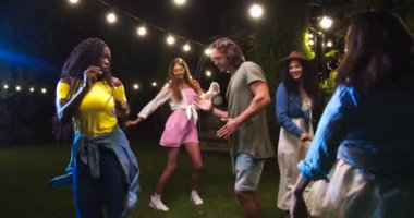Çeşitli etnik çeşitlilikte gençler partide açık havada dans ediyorlar. Afro-Amerikalı neşeli kız ve beyaz adam eğleniyor ve hareket ediyor. Güzel dişiler ve yakışıklı oğlanlar bahçede dans ediyorlar. Eğlenceli konsept
