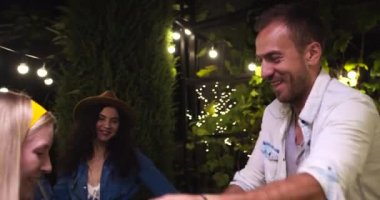 Partide gece vakti bahçede dans eden mutlu beyaz çiftin portresi. Genç güzel kızlar ve yakışıklı oğlanlar açık havada müzik dinliyorlar. Yaz partisi var. Boş zaman konsepti