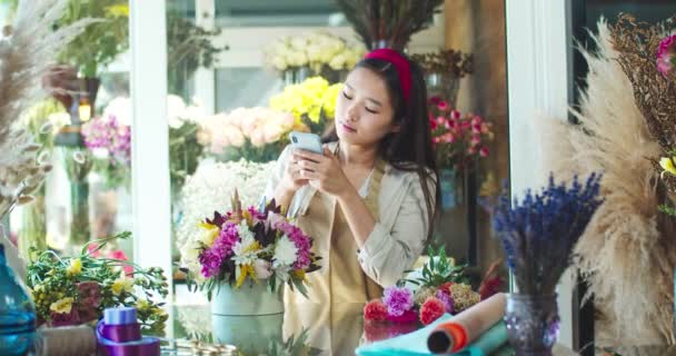 Portrait de belle femme asiatique prenant des photos de fleurs dans le magasin de fleurs. Jolie fleuriste envoyant un message avec photo au client, client. Entreprise, emploi, médias sociaux, concept de nature. — Video