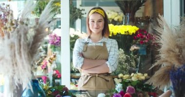 Çiçekçide çalışan önlük giyen çekici bir bayan dükkan sahibi. Çekici beyaz kadın çiçekçi kollarını kavuşturup kameraya bakıyor. İş, girişimcilik, doğa konsepti.