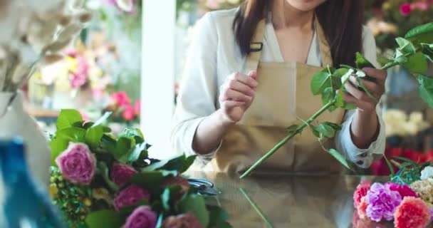 Primer plano de la hermosa florista femenina que usa delantal, trabajando en la tienda de flores moderna. Propietario de una tienda asiática atractiva que toma flores y corta tallos con tijeras. Negocios, concepto de emprendedor. — Vídeos de Stock