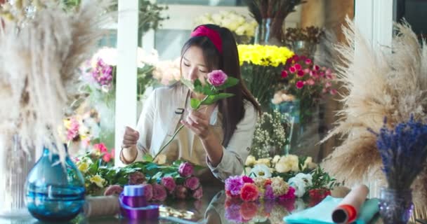 Atractiva florista asiática que trabaja con flores y plantas frescas, de pie en la tienda. Joven vendedora que toma flores y corta tallos en la tienda. Negocios, ocupación, naturaleza, plantas concepto. — Vídeos de Stock