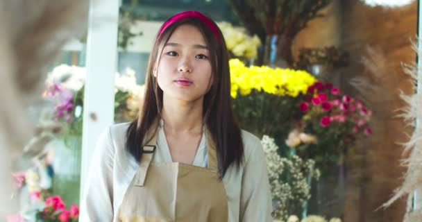 Portret van een mooie Aziatische vrouw in een schort in een bloemenwinkel. Charmin vrouwelijke bloemist in glazen kruising armen, kijken naar de camera en glimlachen. Bedrijfsleven, vrije beroepen, ondernemerschap. — Stockvideo