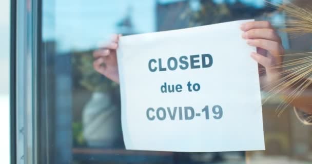 Молодая владелица магазина закрывается во время эпидемии. Красивая женщина-флористка в маске прикрепляет к окну бумагу с текстом "закрыто из-за COVID-19". Пандемия коронавируса. — стоковое видео