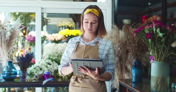 Jolie fleuriste caucasienne travaillant dans un magasin de fleurs moderne. Jolie jeune travailleuse tapant sur tablette, regardant la caméra et souriant. Technologie, affaires, nature, esprit d'entreprise. — Video