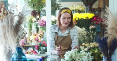 Çiçekçide video çeken önlüklü beyaz kadın blogcu. Güzel bayan çiçekçi takipçiler, izleyiciler ve bitkiler hakkında canlı konferans veriyor. Sosyal medya, vlog, çevrimiçi.