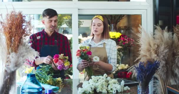 Cheerful young male and female florists working together in flower store. Smiling woman and man workers making bouquets of blossoms, talking to each other and laughing. Commerce, business concept.