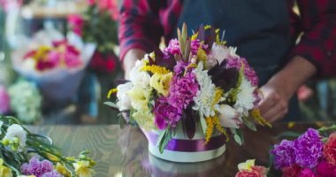 Modern çiçekçide çalışan çekici genç erkek çiçekçi. Dükkanda şapka kutusunun etrafında mor kurdeleyle buket süsleyen yakışıklı beyaz adam. Dekor, iş, ticaret kavramı.