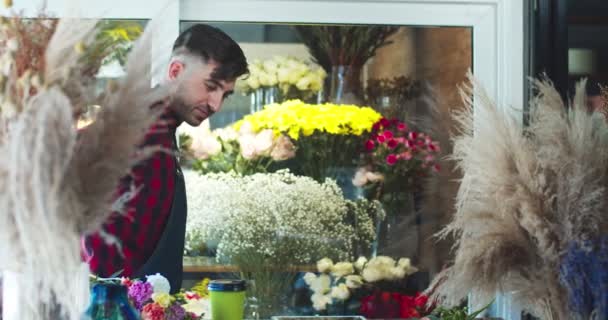 Bonito florista feminina vestindo avental, trabalhando na loja de flores. Bonito jovem caucasiano trabalhador verificando flores na loja. Profissão, profissão, conceito de negócio. — Vídeo de Stock
