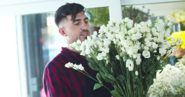 Ritratto di bell'uomo caucasico fiorista che lavora nel negozio di fiori. Bello il giovane operaio che tira fuori vaso con fiori e mette sul tavolo. Business, concetto di commercio. — Video Stock