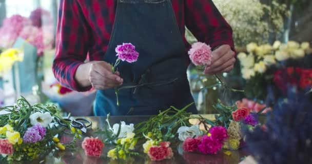 Närbild av snygg ung man florist som arbetar i blomsteraffär. Händer manliga arbetare gör bukett blommor vid bordet. Entreprenörskap, företag, yrke, yrkesidé. — Stockvideo