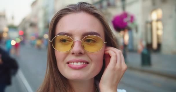 Close up retrato da bela mulher caucasiana feliz colocando fones de ouvido sem fio e dança. Menina muito alegre em óculos de sol ouvindo música e se movendo ao ar livre na cidade. Conceito de emoções — Vídeo de Stock