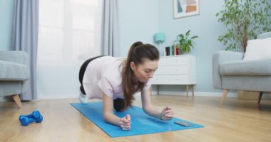 Formda bir kızın zamanlayıcıyı açması ve evde spor yapmaya başlaması. Esmer, kalas pozisyonunda kalıyor. Sağlıklı ve spor yaşam tarzı. Eğitim, egzersiz ve sağlık..