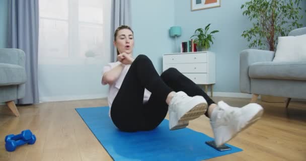 Plan intermédiaire de jeune fille en forme faisant des exercices dans son appartement confortable. Femme faisant abdominaux exercices flexion des jambes sur le sol à la maison. Style de vie sain et sportif. Concept de formation, entraînement et bien-être — Video