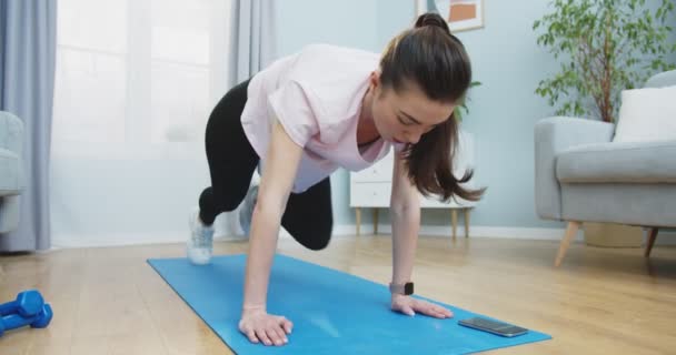 Środkowy plan młodej dziewczyny robi trening fitness dla zdrowego stylu życia i silny brzuch w domu. Bieganie w pozycji deski przy użyciu stopera w telefonie. Zdrowy i sportowy styl życia. — Wideo stockowe