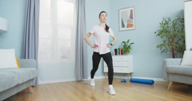 Formda güzel bir kadının spor yaptığı ve sağlıklı bir yaşam tarzı için egzersiz yaptığı ve güçlü bacakları olduğu orta plan evdeki oturma odasında kaslıdır. Spor ve spor. Eğitim, egzersiz ve sağlık..