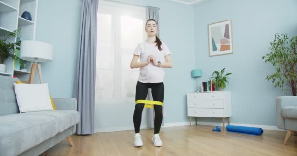 Middle plan of fitness female enjoying training with resistance band at home. Sporty woman doing exercises with elastic band, making steps during butt-focused workout. Healthy and sport lifestyle. — Video Stock