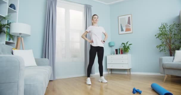 Midden plan van sportieve vrouw training ochtend training in huis interieur. Jonge vrouw doet fitnesstraining in huis. Meisje leunend naar rechts en links, warm-up. Gezonde en sportieve levensstijl. — Stockvideo