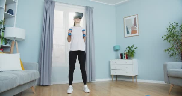Plan intermédiaire de la jeune femme sportive portant des lunettes de réalité virtuelle et effectuant des mouvements de boxe lors de l'entraînement à la maison avec des haltères. Sport et fitness. Concept de formation, entraînement et bien-être. — Video