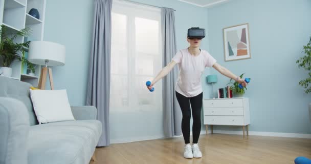 Midden plan van jonge vrouw training thuis en het dragen van virtual reality brillen met behulp van halters. Gezond levensstijl en vr simulatie concept. Sport en fitness. Training, training en wellness. — Stockvideo