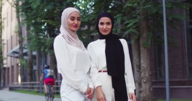 Geleneksel türbanlı iki Arap kadının caddeye bakıp gülümserken orta plan çekimleri. Şehirde tesettüre girmiş güzel müslüman kadınlar. Şık beyaz kıyafetli İslami mutlu bayanlar..