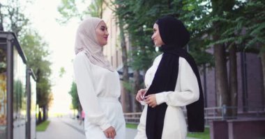 Geleneksel türbanlı iki genç müslüman kadının konuşmalarının ve caddede kameraya bakmalarının orta plan çekimi. Şehirde tesettürlü güzel Arap kadınlar.