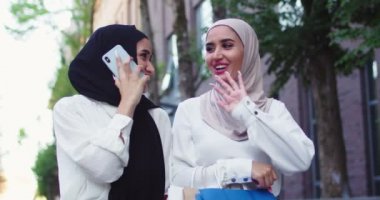 Geleneksel türban takmış, telefonda konuşan ve dükkandan çanta taşıyan iki Arap kadının portrelerini yakından çek. Alışveriş ve kahkahalardan sonra cep telefonuyla konuşan kadın başörtüsü..