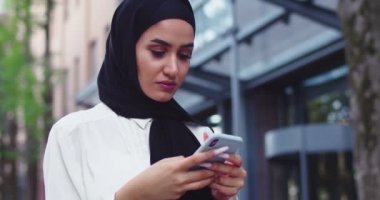 Geleneksel türbanlı, telefona bakıp gülümseyen Arap kadının portresini yakından çek. Güzel Müslüman kadın tesettürde mesajlar okuyor, mesajlaşıyor, akıllı telefondan internette geziniyor..