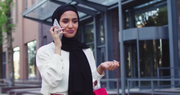 Close up of Arabic beautiful woman in traditional headscarves speaking on phone walking at street. Pretty muslim female in hijabs making call at city centre after shopping. — Stock Video