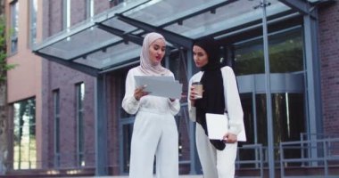 Geleneksel türbanlı kendine güvenen iki Müslüman kadın açık havada dokümanları tartışıyor, konuşuyor, kahve içiyor. İş birliğini tartışan profesyonel iş arkadaşları. Takım çalışması, iş, yaşam tarzı.