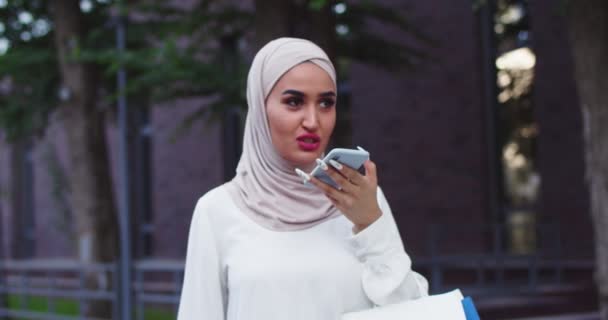 Close up portrait of Arabic woman in traditional headscarves recording voice messages. Pretty muslim female in hijabs texting, talking with online consultant using smartphone after shopping. — Stock Video