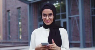Geleneksel başörtüsü ve gözlüklü, telefona ve kameraya bakan genç ve güzel bir Arap kadını yakından çek. Caddedeki tesettürlü neşeli Müslüman bayanı yakından çek. İslami cazibeli mutlu bayan