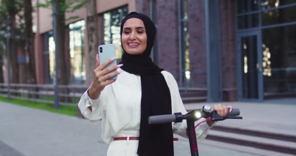 Молоді арабські красиві жінки в традиційних газетних хустинках, відеоблозі, роблять селфі з електричним скутером, зустрічаються з другом на вулиці. Красиві аравійські жінки в хіджабах у місті.. — стокове відео