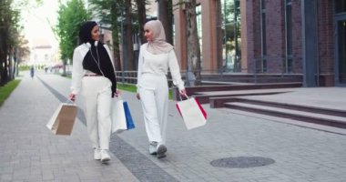 İki kendine güvenen genç Arap kadın tesettüre girmiş. Müslüman kadınlar gülümsüyor, tartışıyorlar, konuşuyorlar, bir şehrin caddesinde yürüyorlar, ellerinde alışveriş torbaları, boynunda beyaz kulaklıklarla..