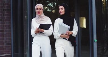 Başörtüsü takan iki güzel Arap kadının orta plan çekimi. Merdivenlerden birlikte kâğıtlarla iniyorlar, konuşuyorlar. Modern yaşam tarzı, teknoloji, iş tartışmaları