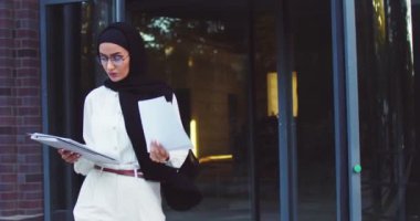 Üniversite bahçesinde tablet ve kağıtlarla yürüyen kendine güvenen gözlüklü Müslüman kadın portresi. Avrupa 'da okuyan genç bir göçmen kadın. Modern Orta Doğulu bayan yurtdışında eğitimin tadını çıkarıyor