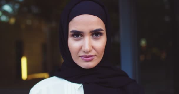 Primer plano retrato de la joven árabe hermosa mujer en el pañuelo de cabeza tradicional mirando a la cámara. Primer plano de bastante alegre musulmana hembra en hijab en la calle. Al aire libre. Islámica encantadora dama feliz — Vídeos de Stock