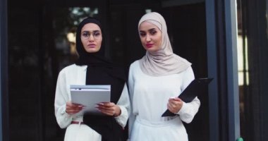 Geleneksel başörtüsü ve gözlüklü, kameraya bakan ve elinde belgelerle gezen iki Arap iş kadınının portresini yakından çek. Caddede tesettürlü oldukça neşeli Müslüman kadınlar..